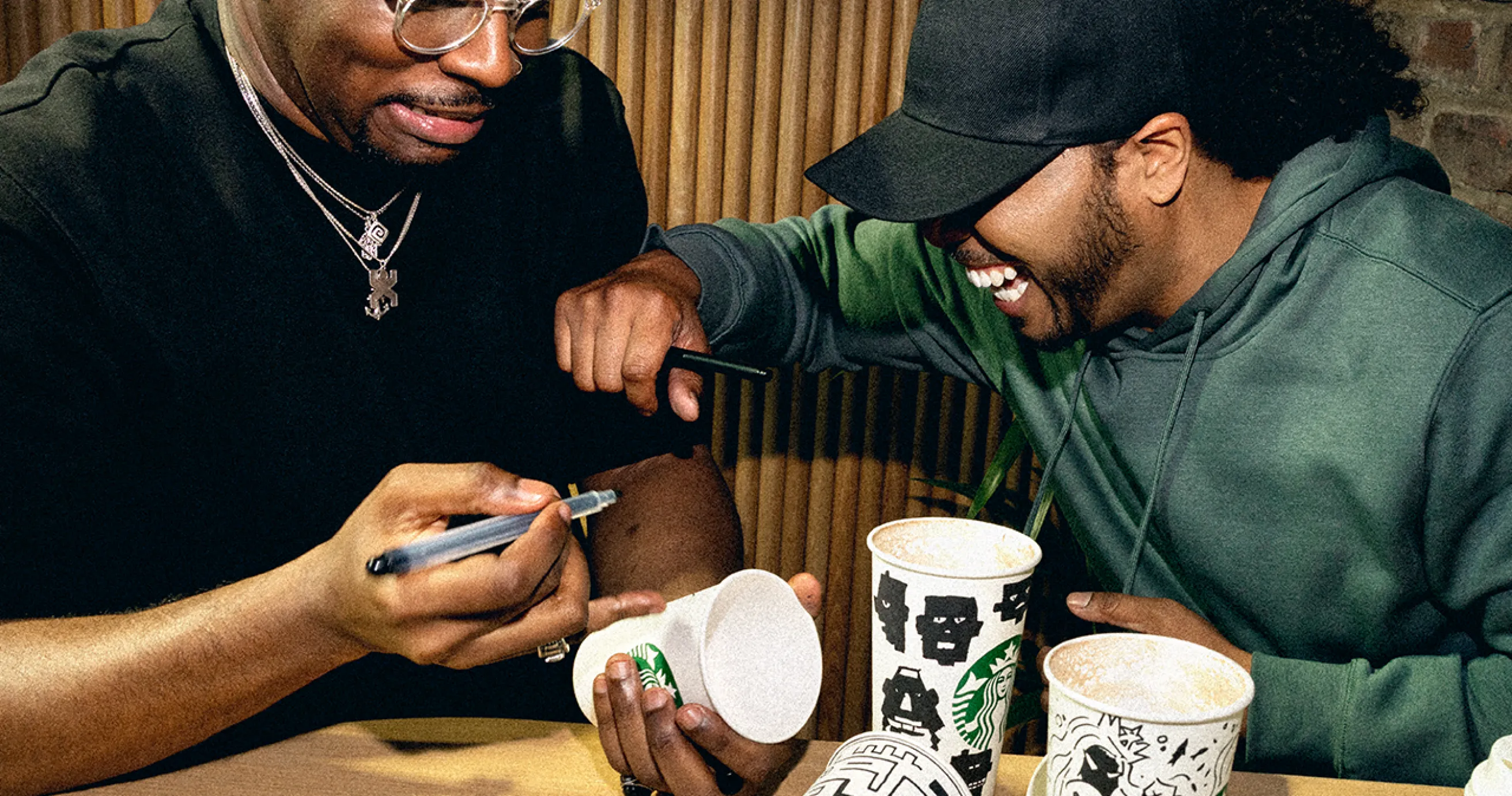 Two fans drawing on Starbucks Cups and laughing together