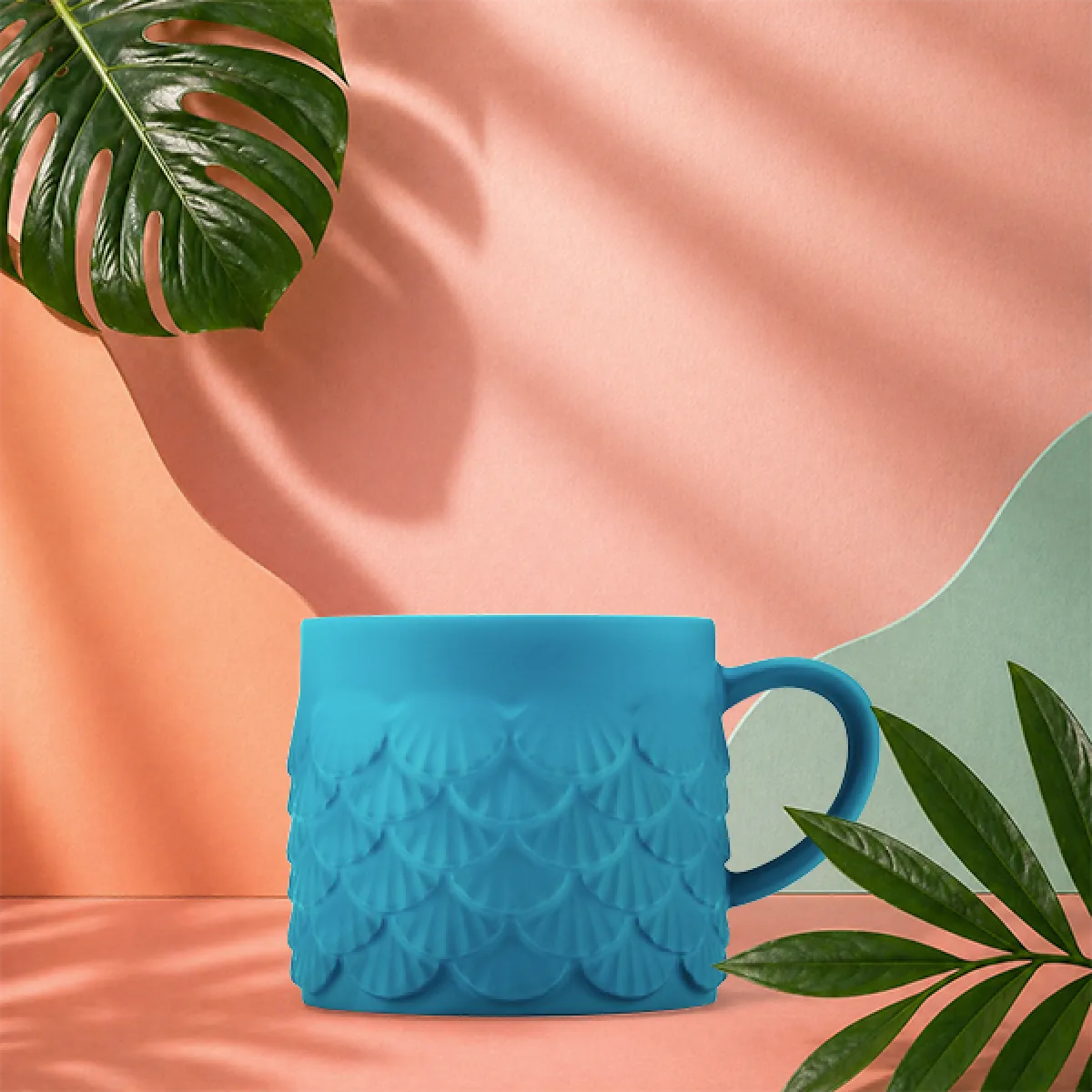 A photo of our new summer siren shell mug - with a soft touch finish in a mid-blue and textured, layered shell shaped scales decorating the outside.