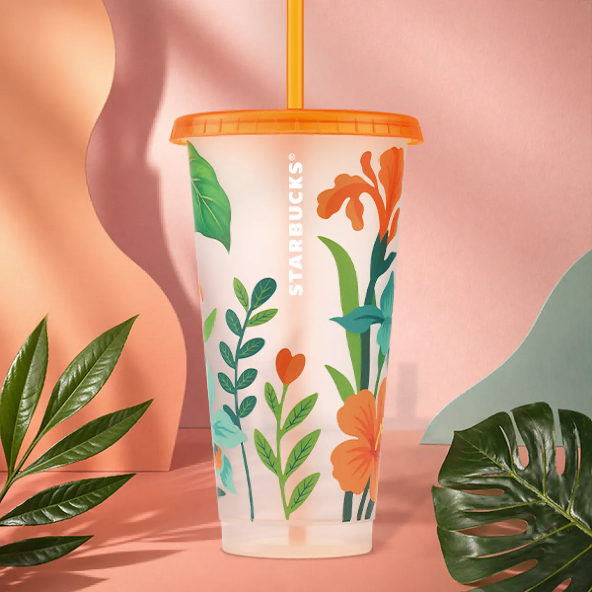 A photo of our new plastic reusable cold cup. This seasons design features bold, brightly coloured florals on a transparent background, with a bright orange lid and straw to match. 