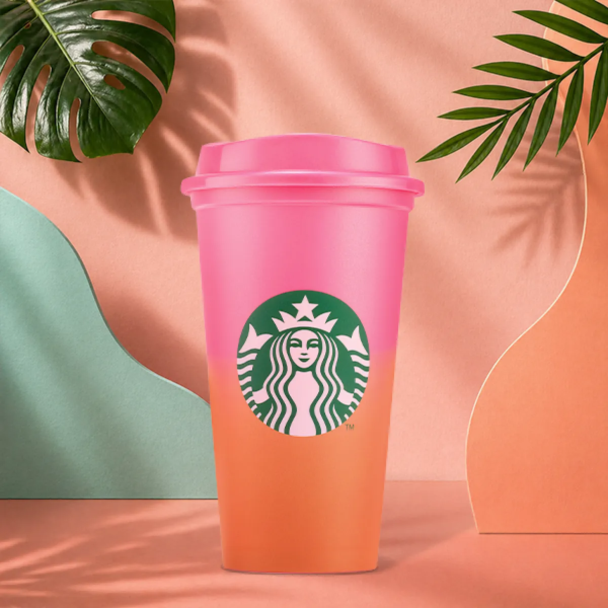 A photo of our new reusable hot cup for the season. The classic Starbucks takeaway cup, but in a bright pink to orange ombre, complete with pink lid