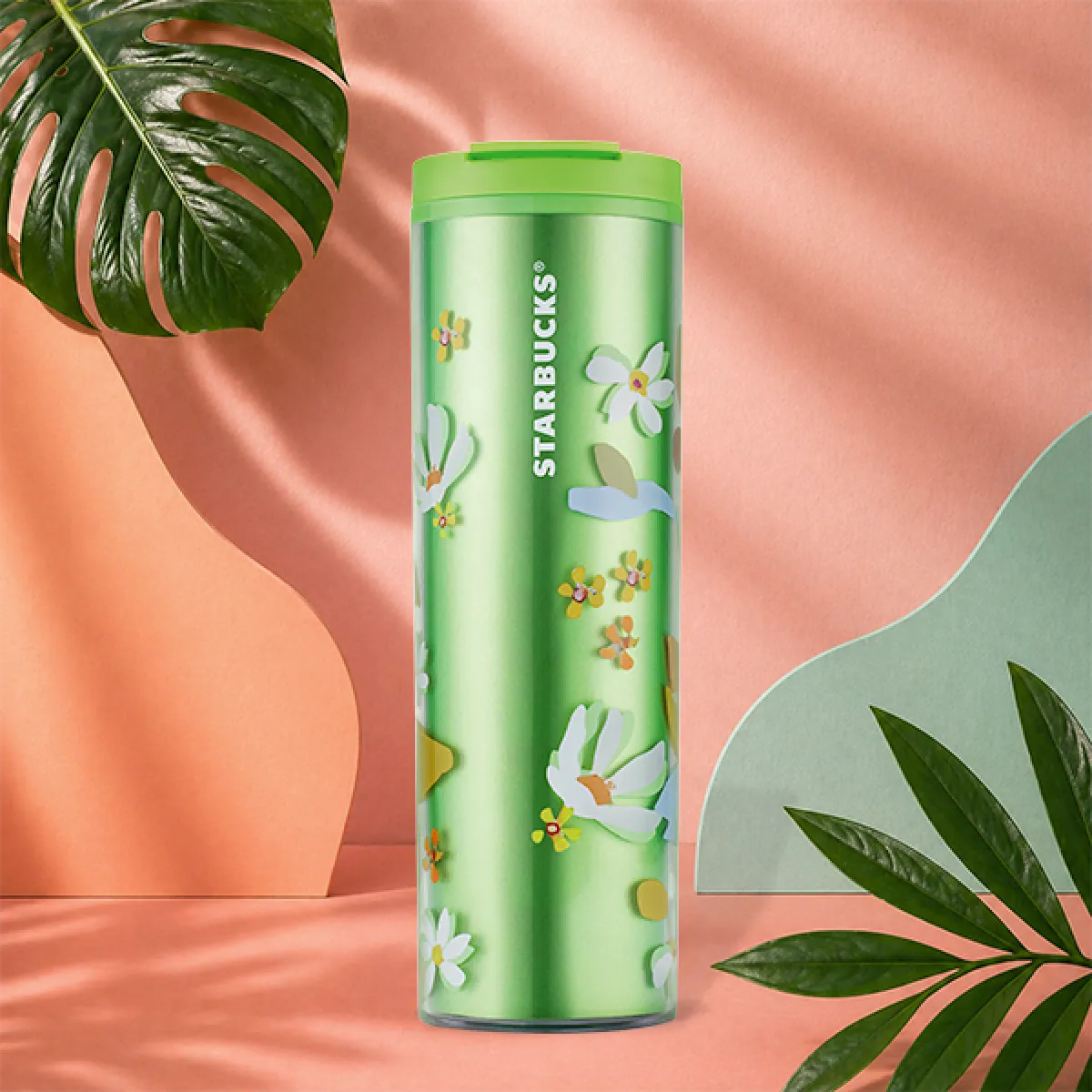 A photo of our new summer Floral green tumbler. A sleek green, cylindrical design with white, orange and yellow flowers covering the outside, and a green click lid. 