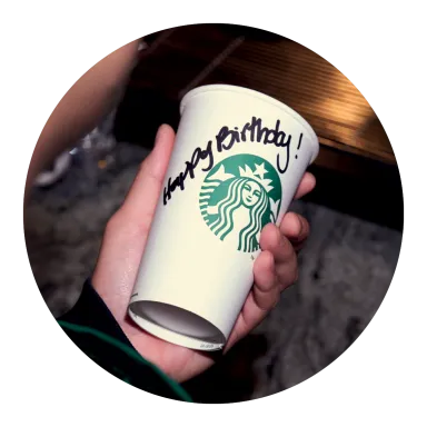 A close up photo over a barista's shoulder of a Starbucks cup with "Happy birthday" written in Sharpie