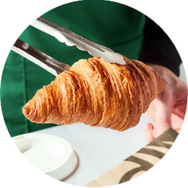 A photo of a fresh, flakey butter croissant being served with tongs.