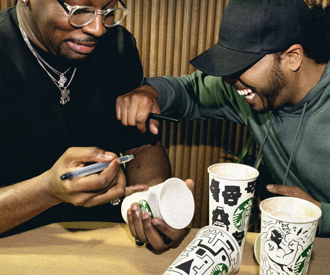 Two friends laugh whilst sketching on Starbucks takeaway cups