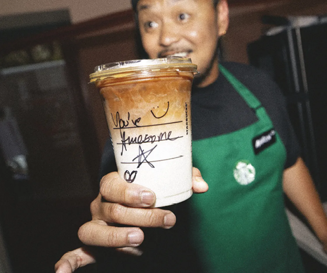 Starbucks Barista holding a takeaway cup to camera that says 'You're awesome'