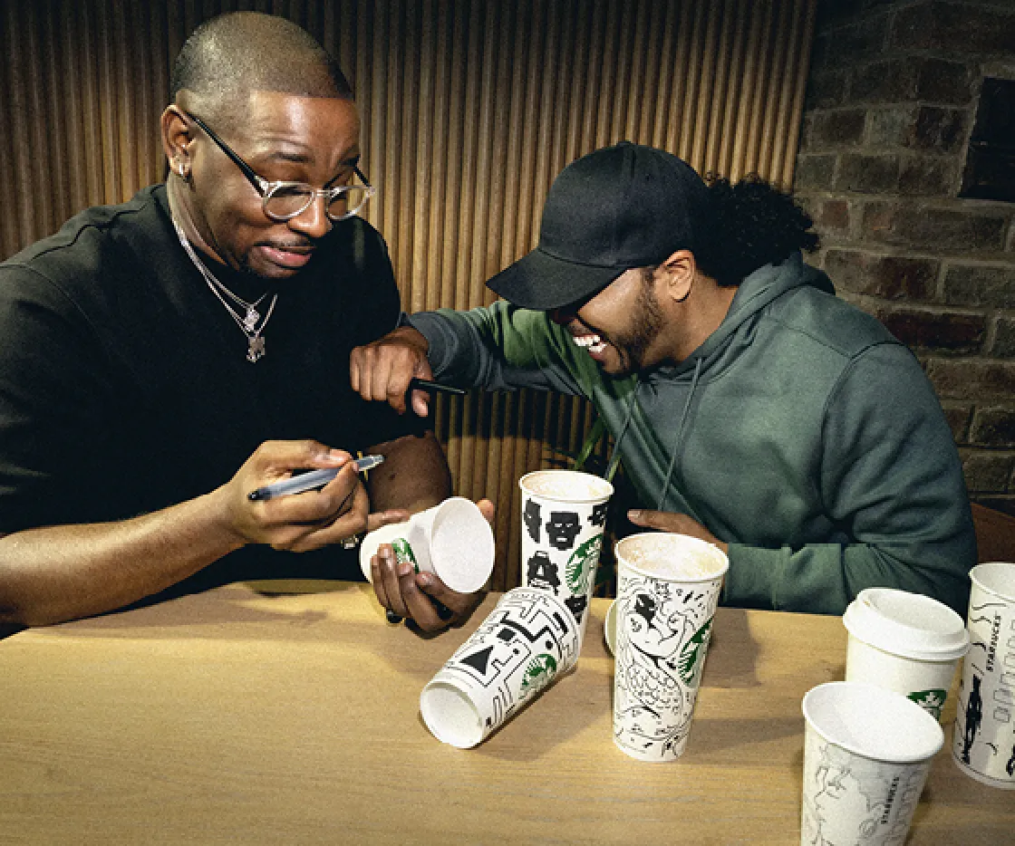 Two friends laugh whilst sketching on Starbucks takeaway cups