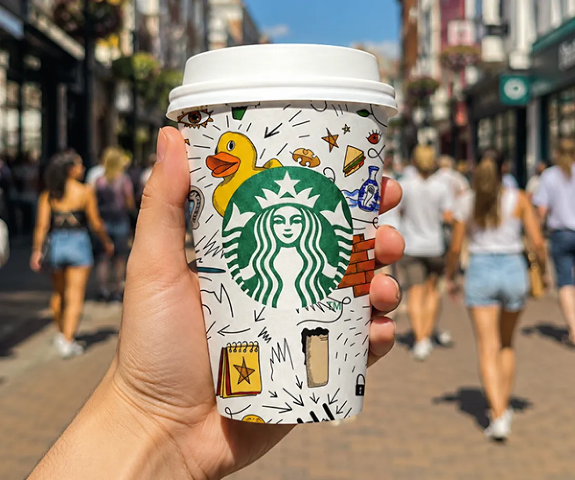 Lifestyle shot of illustrated Starbucks cup being held by it's designer
