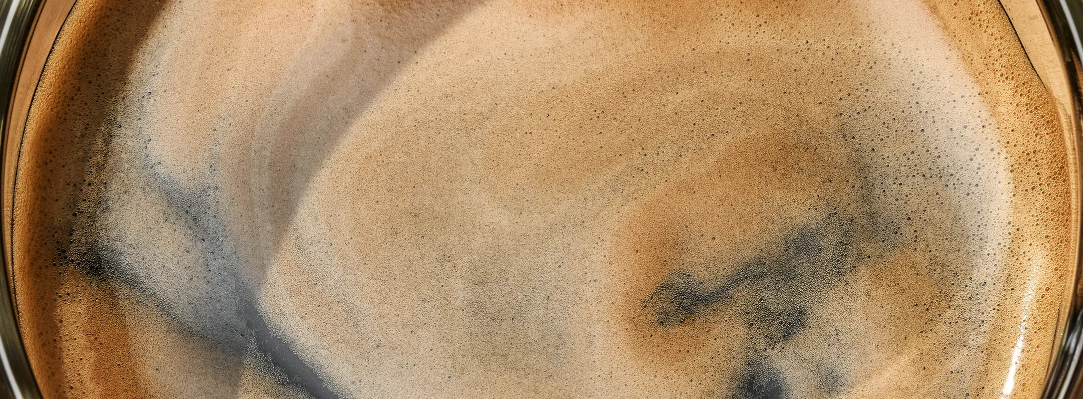 A close up photo of the coffee crema on top of a fresh hot black coffee