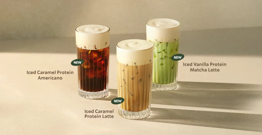 Three iced drinks topped with thick, creamy protein cold foam sit on a light countertop. The drinks include an americano, latte, and a matcha from Starbucks.