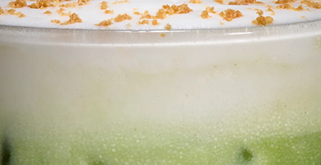 A close up photo of the top of an iced apple crumble matcha latte, with cold foam and sprinkles. 